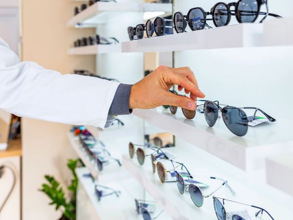 Person selecting sunglasses from a display shelf.