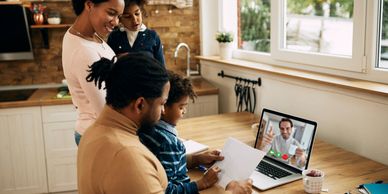 Family video calling a man on a laptop in a cozy kitchen.