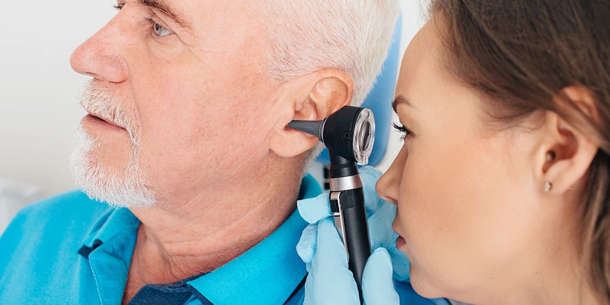 Doctor examining elderly man's ear with an otoscope.