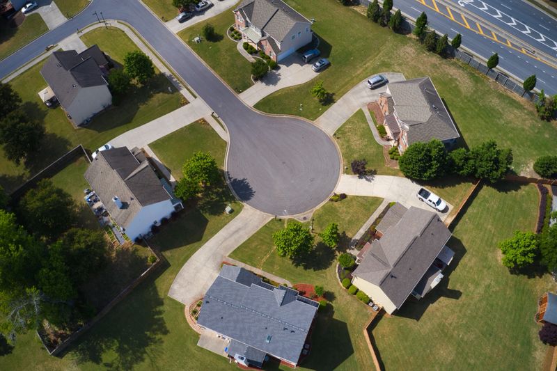 Shot using a drone during the golden hour shows an upscale suburbs with gold course, lake, houses and roof tops