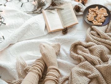 Cozy winter scene with warm socks, knitted blanket, book, and gingerbread cookies.