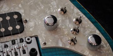 Close-up of an electric guitar's knobs and pickup.