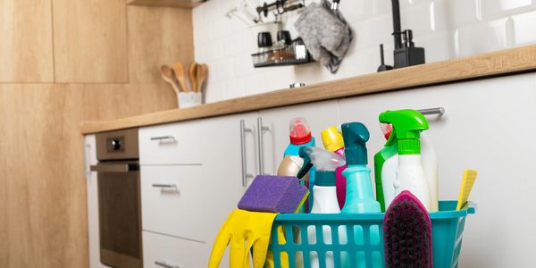 Basket of assorted cleaning supplies on kitchen counter.