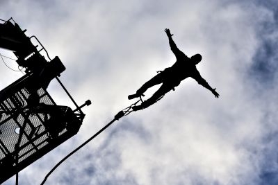 Person bungee jumping with arms outstretched against cloudy sky.