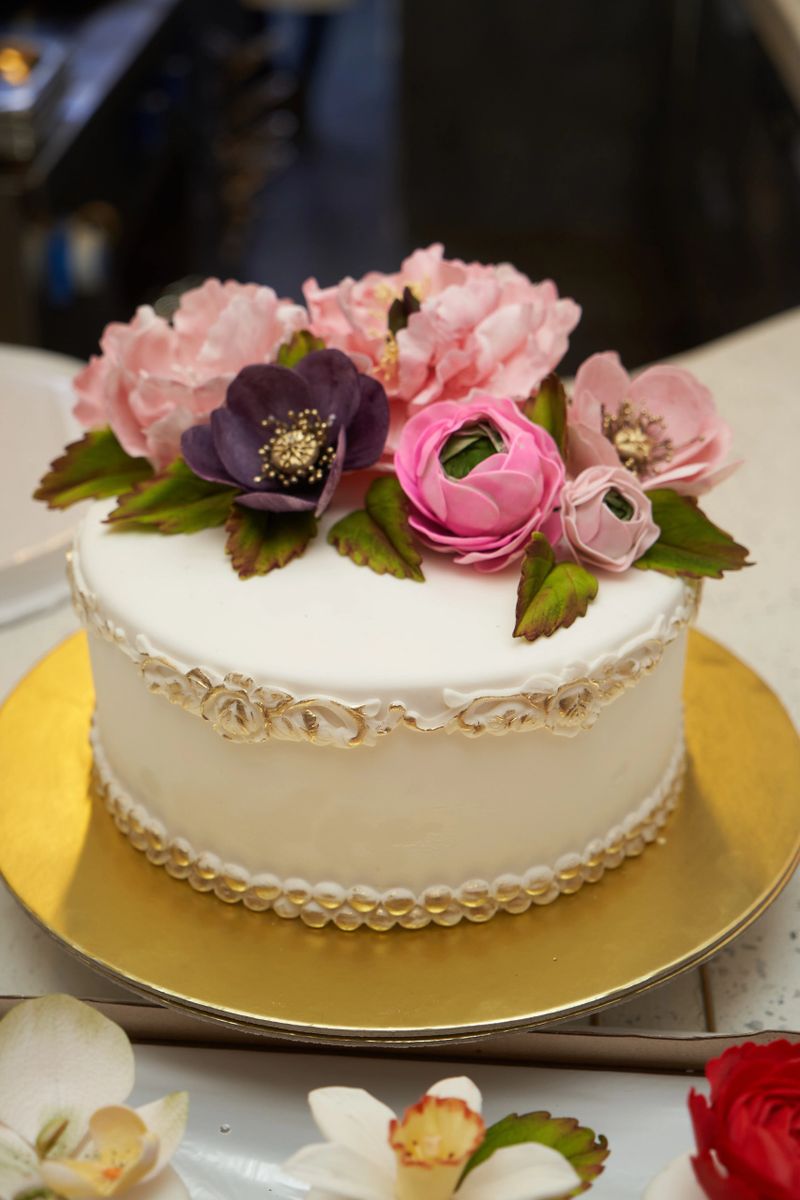 White cake with pink flowers on golden tray. Cake decorated with flowers