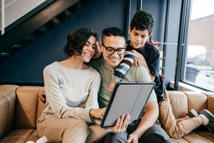 A happy family enjoys time together looking at a tablet on a couch.