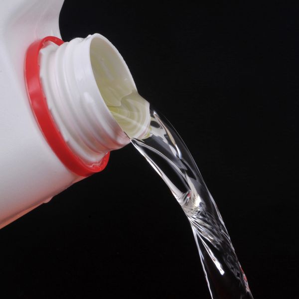 Water pouring from a white plastic bottle against a black background.