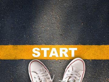 White sneakers standing at a yellow start line on asphalt.