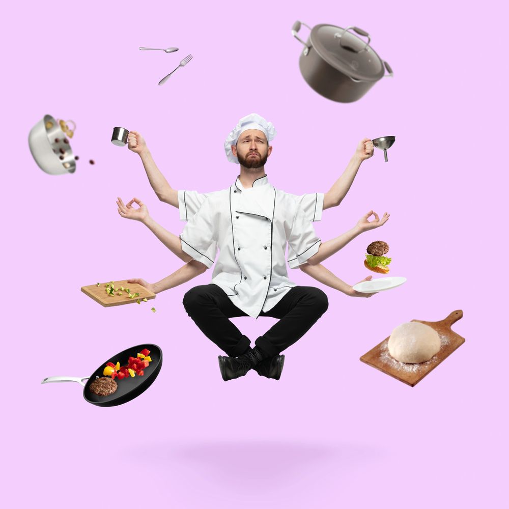 A meditating chef with six arms juggling cooking utensils and food items.