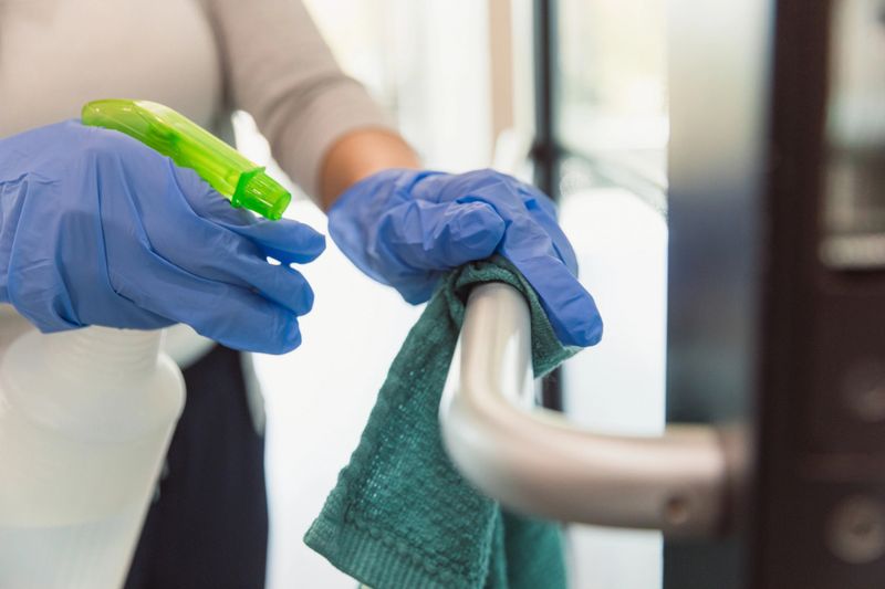 A female custodian wears protective gloves as she cleans a hand rail in an office during COVID-19