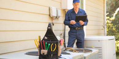 Technician with tools working on an outdoor HVAC unit.