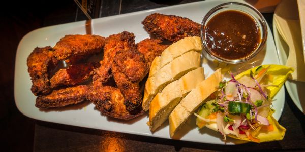 Plate of crispy fried chicken wings with bread, barbecue sauce, and a fresh salad.
