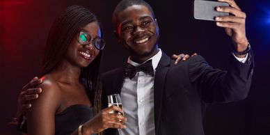 A well-dressed couple takes a selfie, smiling and holding a champagne glass.