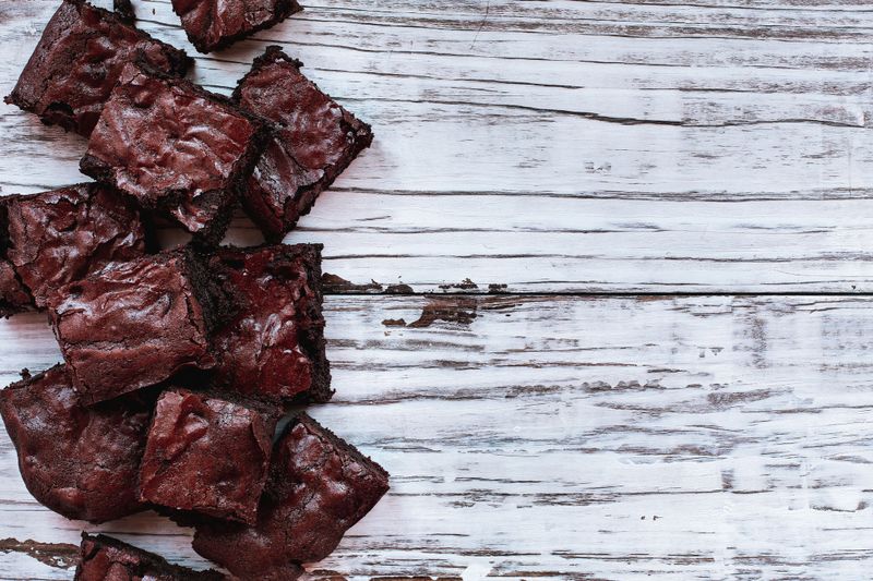 Squares of delicious, homemade fudgy brownies stacked a white rustic wooden table background. Image shot from top view overhead.
