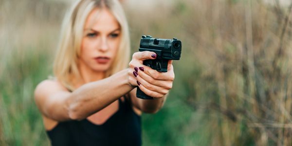 Woman aiming a gun outdoors.