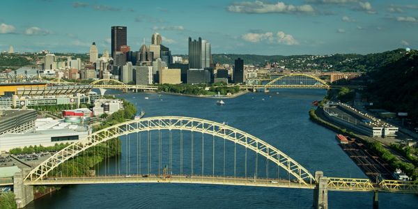 City skyline with yellow bridges over a river under a blue sky.