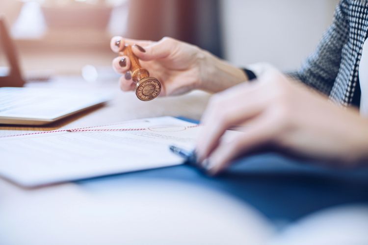 Woman using a wax seal stamp on paper beside a lit candle.