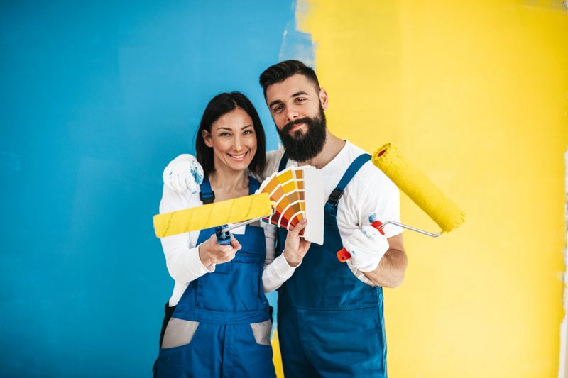 Happy couple renovating their home. They are together painting a wall in blue or teal and yellow colors.