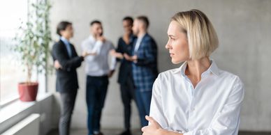 A woman in a white shirt looks away while three men converse in the background.