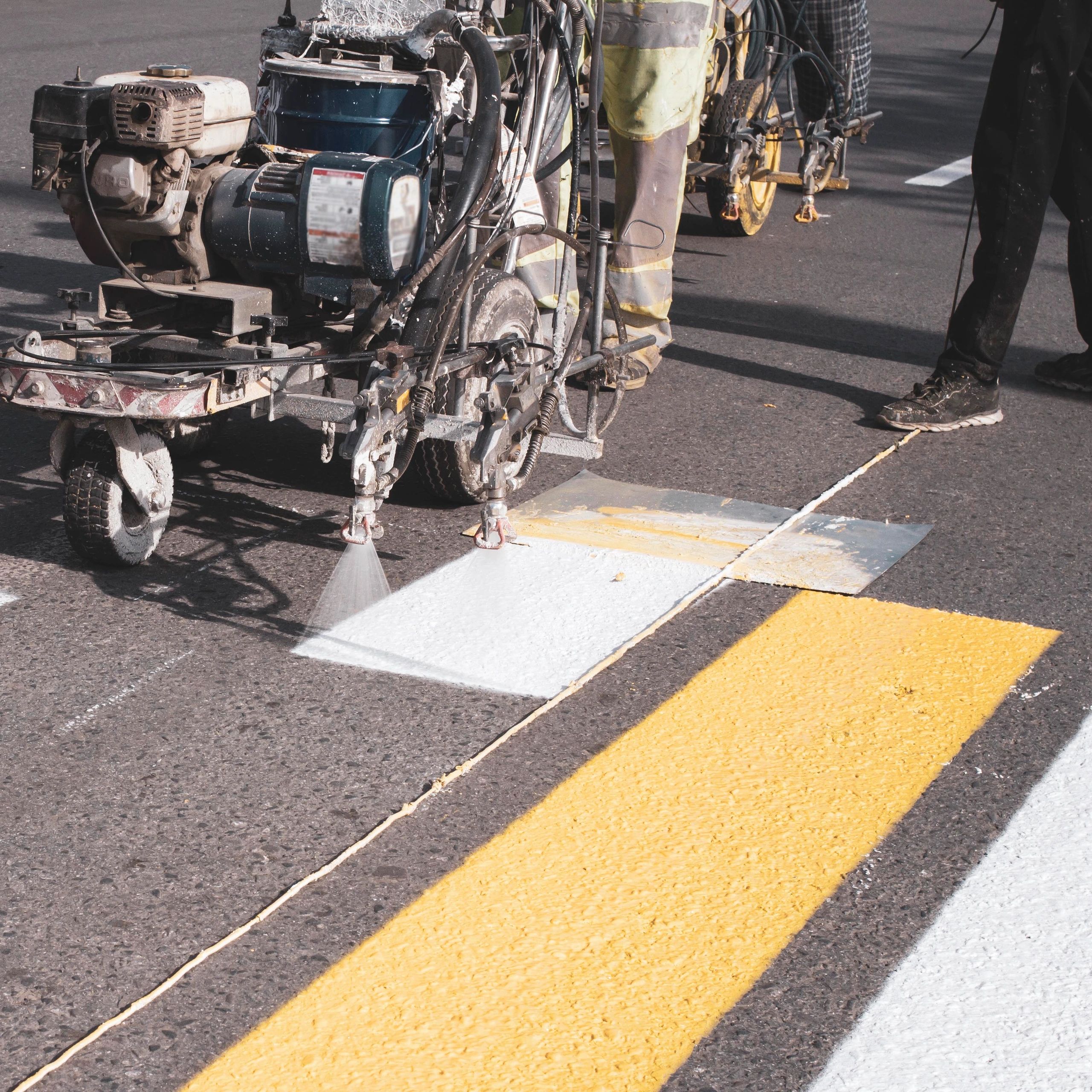 Machine painting white lines on a road with yellow lines beside it.