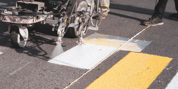Machine painting white road markings on asphalt near yellow lines.