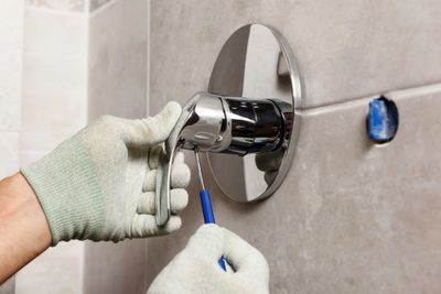 A person installs a chrome shower handle on a tiled wall.