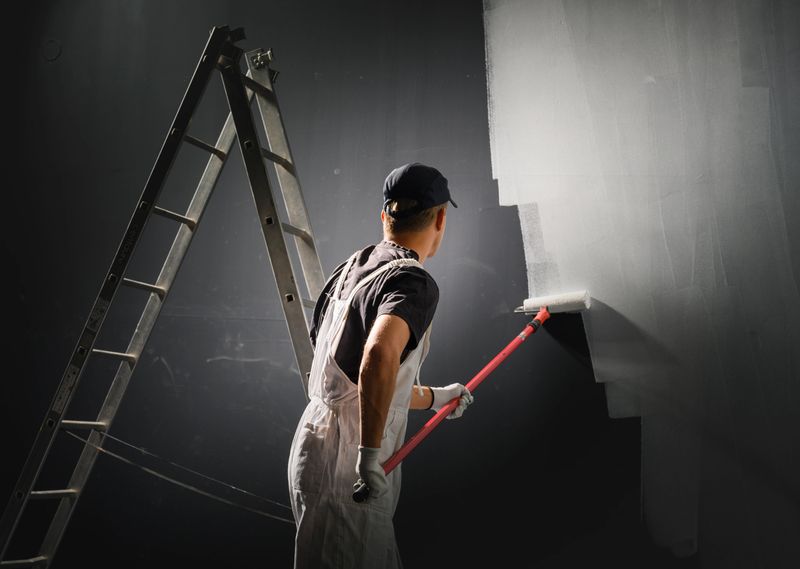 Male decorator painting a wall with white color.