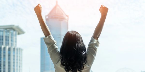 Confident woman with her arms up and facing tall buildings representing leadership and career growth