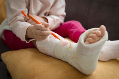 Child coloring on a leg cast with an orange marker.