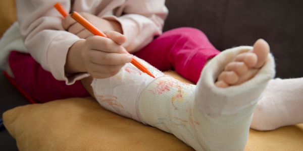 Person coloring on a leg cast with an orange marker.