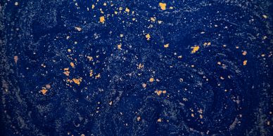Abstract blue surface with scattered gold flakes creating a cosmic effect.