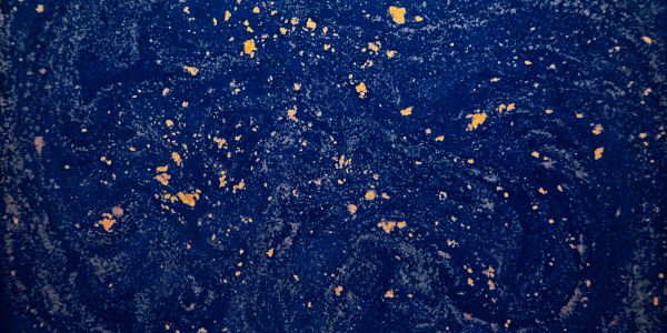 Abstract blue surface with scattered gold flakes creating a cosmic effect.