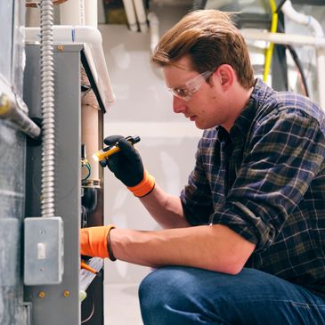 Man fixing a furnace while wearing safety glasses and gloves.