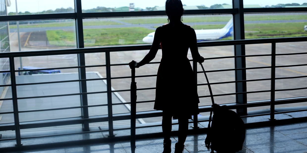 Silhouette of a woman with luggage and umbrella at an airport window.