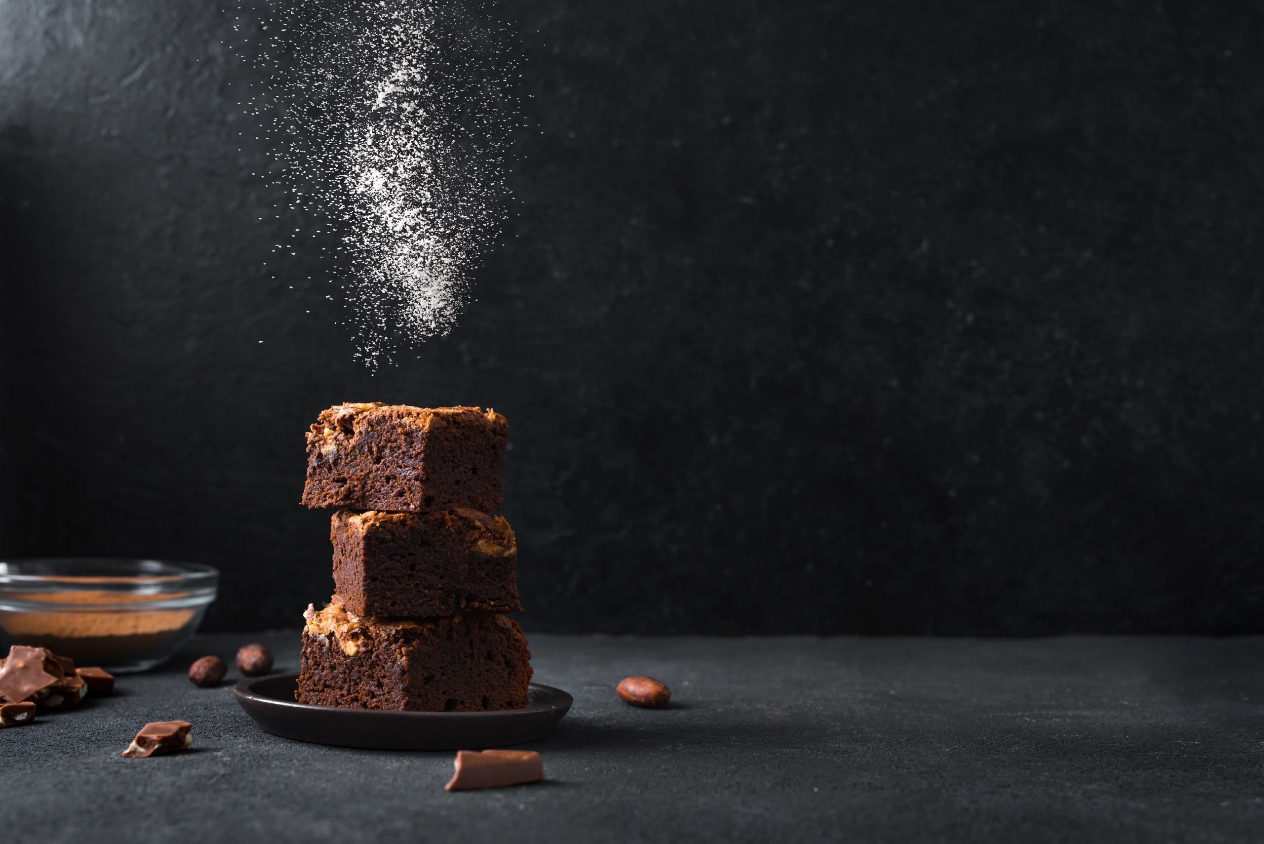 Stack of three chocolate brownies with powdered sugar falling on them.