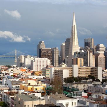 San Francisco skyline with the Transamerica Pyramid and Bay Bridge under a partly cloudy sky.