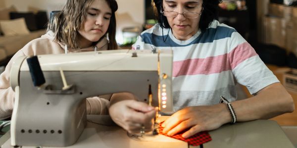 A woman teaching a girl to sew on a sewing machine.