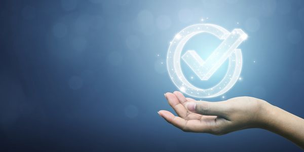 Hand holding a glowing digital checkmark symbol on a blue background.