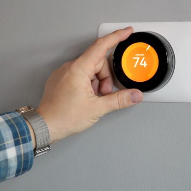 Person adjusting a smart thermostat set to 74 degrees heating.