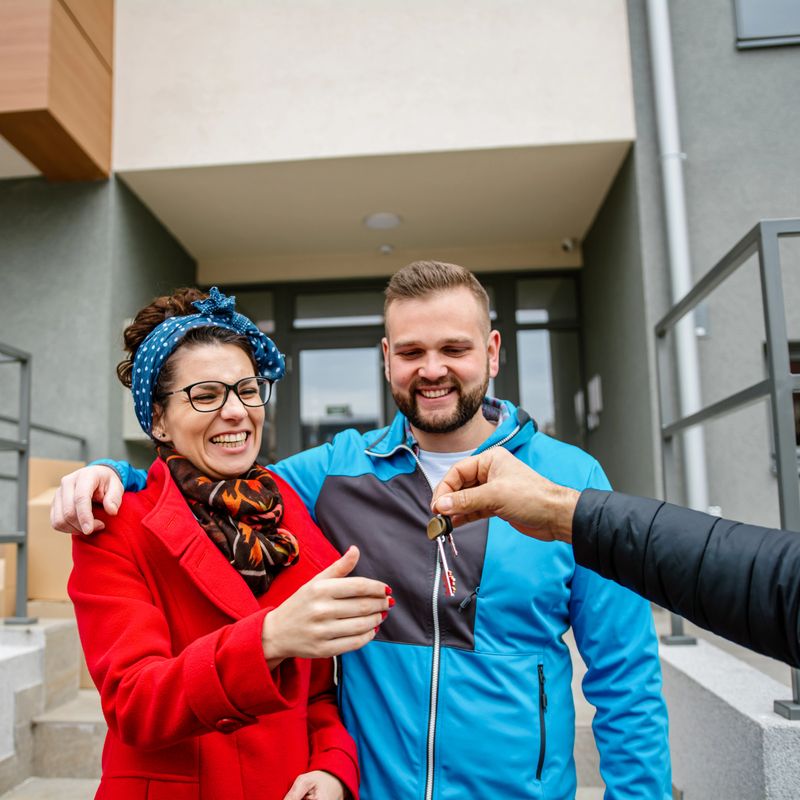 Happy couple is taking keys from their new apartment from real estate agent. Hands of estate agent giving keys to the couple. The agent handed the keys a young couple