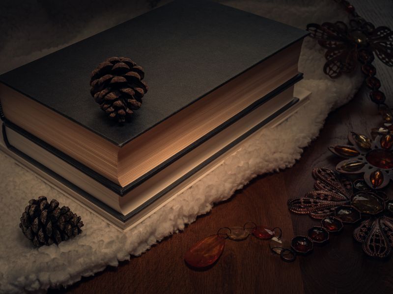 Hardback books on a cosy blanket with pone cones on a mahogany table
