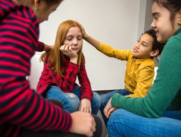 Children comforting a sad girl in a supportive group setting.