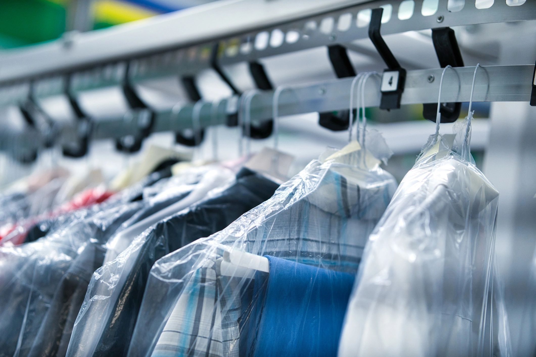 Clothes covered in plastic hanging on a rack, likely at a dry cleaner.