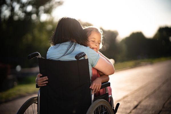 A child warmly hugging a person in a wheelchair outdoors during sunset.