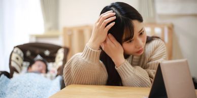 A woman fixing her hair while a baby sleeps in the background.