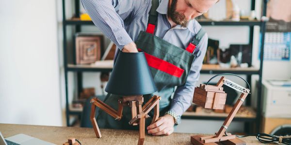 Man assembling wooden lamp models in a workshop.