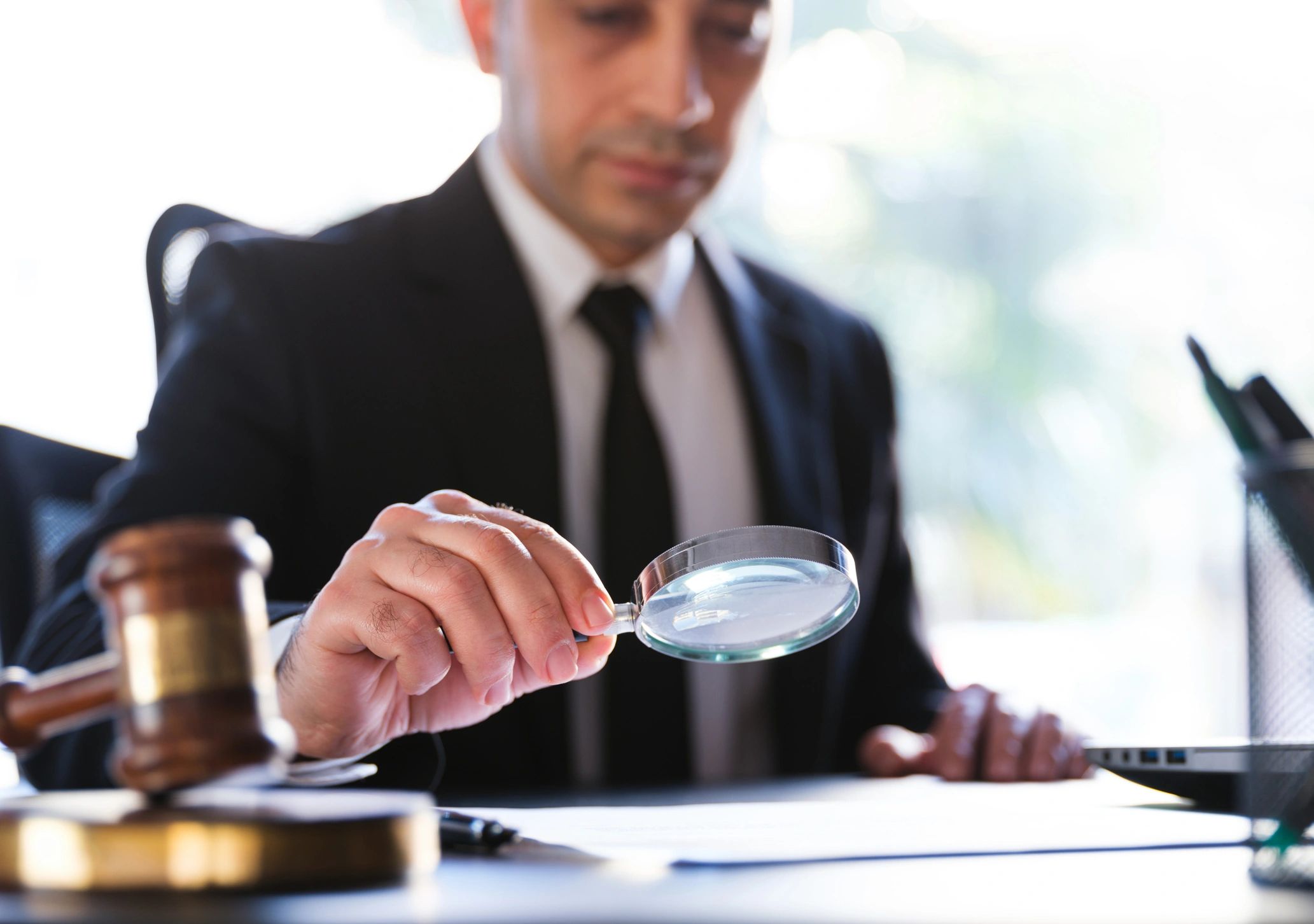Man in suit examining documents with magnifying glass.