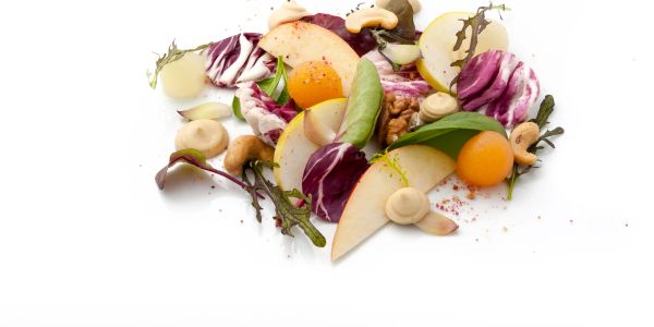 Artistic salad with fresh fruits, nuts, and leafy greens on white background.