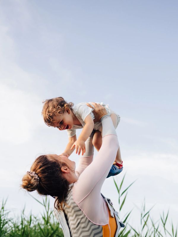 Mother joyfully lifting her toddler against a clear sky.