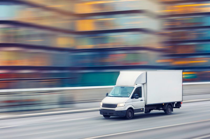 A delivery truck travelling fast on a city street with motion blurred office buildings in the background.